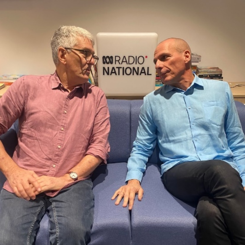 two older men look at each other on a couch with a radio national sign behind them